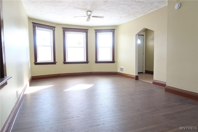 empty room with ceiling fan, dark hardwood / wood-style flooring, a textured ceiling, and a wealth of natural light