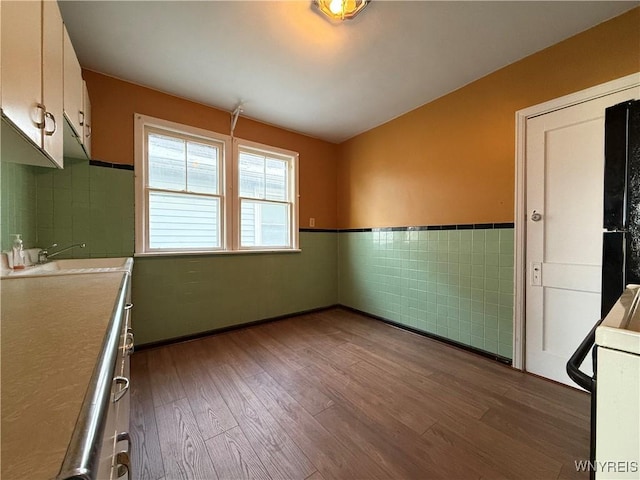 kitchen with hardwood / wood-style flooring, white cabinetry, sink, and tile walls