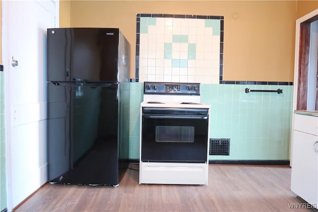 kitchen with range with electric stovetop, black fridge, tile walls, and light hardwood / wood-style floors