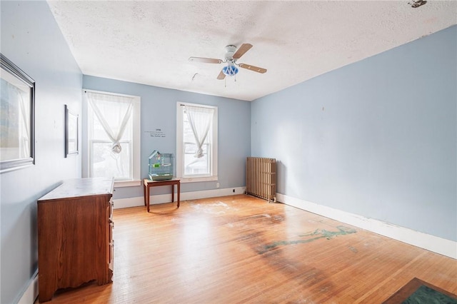 interior space featuring ceiling fan, radiator, a textured ceiling, and light wood-type flooring