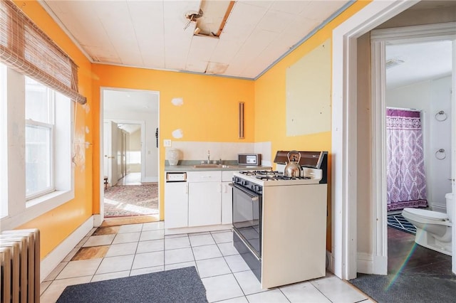 kitchen with light tile patterned floors, gas range, radiator heating unit, and a wealth of natural light