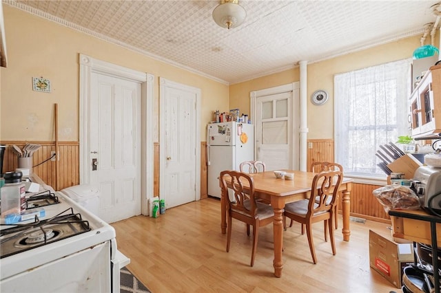 dining space featuring crown molding, light hardwood / wood-style flooring, and wood walls