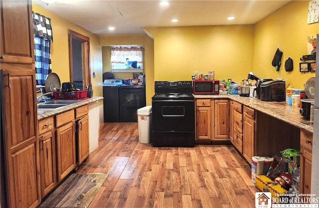 kitchen featuring sink, light hardwood / wood-style flooring, black range with electric cooktop, light stone countertops, and washer and clothes dryer