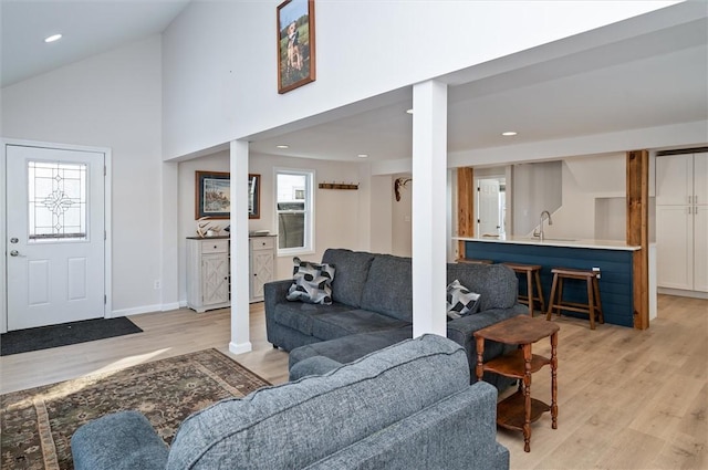 living room featuring high vaulted ceiling, sink, and light wood-type flooring