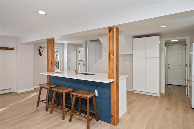 kitchen featuring a kitchen bar, sink, white cabinets, and light wood-type flooring