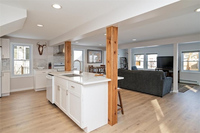 kitchen with sink, white cabinetry, an island with sink, decorative backsplash, and wall chimney range hood