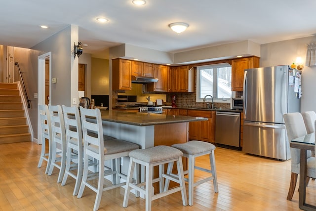 kitchen with light wood-type flooring, stainless steel appliances, kitchen peninsula, sink, and dark stone countertops