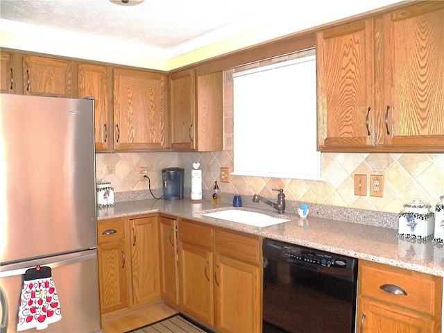 kitchen featuring stainless steel refrigerator, dishwasher, sink, backsplash, and light stone counters