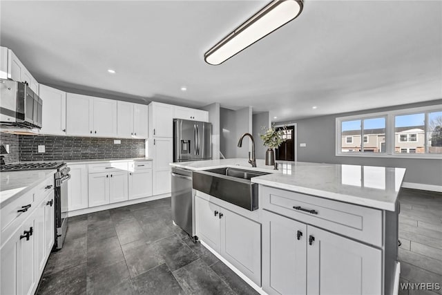 kitchen with sink, a kitchen island with sink, stainless steel appliances, light stone countertops, and white cabinets