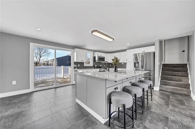 kitchen featuring a kitchen island with sink, stainless steel appliances, a breakfast bar, and white cabinets