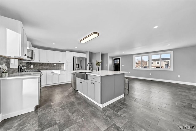 kitchen with appliances with stainless steel finishes, white cabinetry, sink, a kitchen bar, and a kitchen island with sink