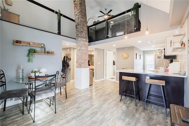 kitchen with a kitchen bar, white cabinetry, light hardwood / wood-style flooring, kitchen peninsula, and a high ceiling