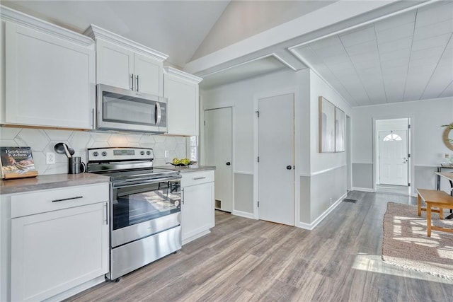 kitchen featuring white cabinetry, stainless steel appliances, tasteful backsplash, vaulted ceiling, and light wood-type flooring