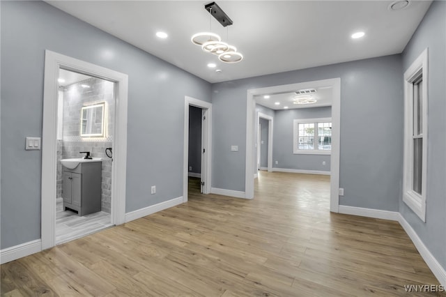 empty room with sink, light hardwood / wood-style flooring, and a notable chandelier