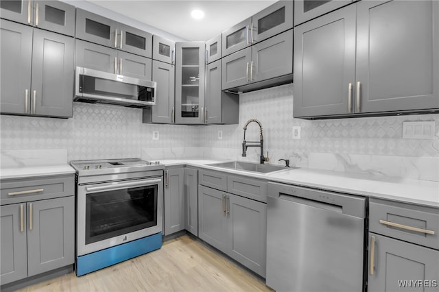 kitchen featuring sink, gray cabinetry, light stone counters, appliances with stainless steel finishes, and light hardwood / wood-style floors