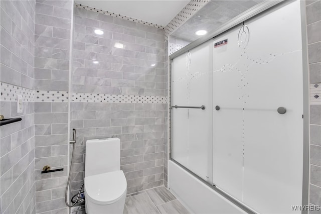 bathroom featuring shower / bath combination with glass door, toilet, and tile walls