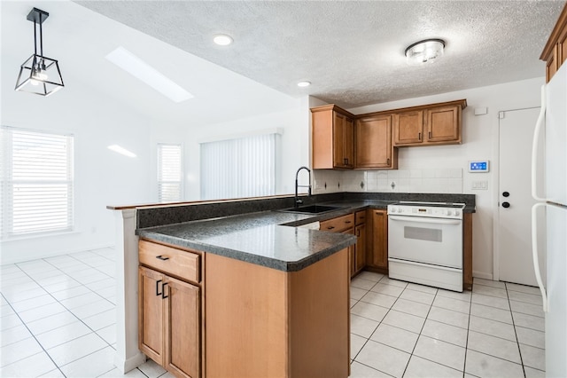 kitchen featuring sink, white appliances, vaulted ceiling with skylight, decorative light fixtures, and kitchen peninsula