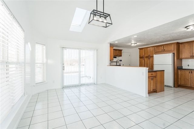 kitchen featuring sink, hanging light fixtures, lofted ceiling with skylight, light tile patterned flooring, and white fridge