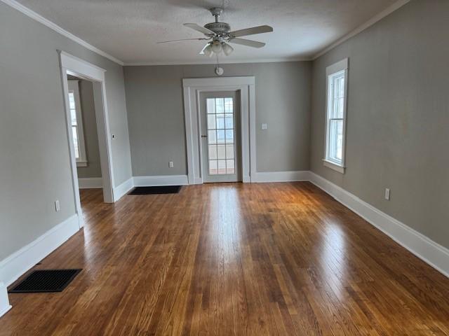 empty room featuring visible vents, a healthy amount of sunlight, dark wood-type flooring, and ornamental molding