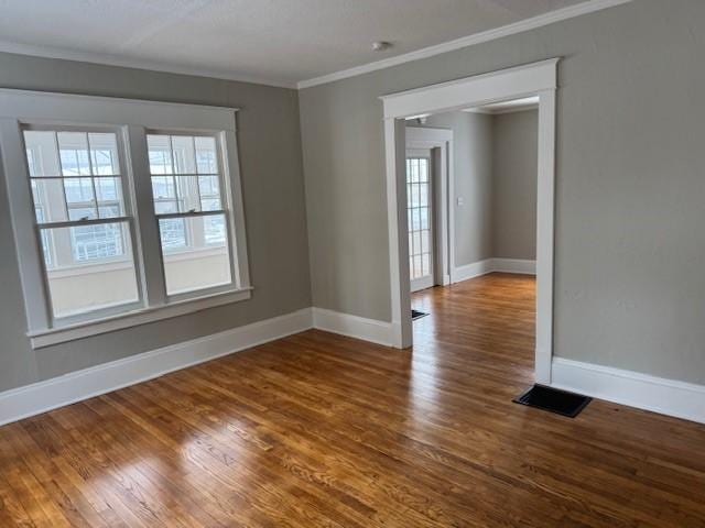 spare room featuring crown molding, dark wood-style flooring, and a wealth of natural light