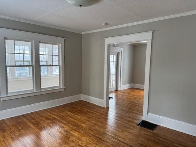 spare room featuring visible vents, a textured ceiling, wood finished floors, crown molding, and baseboards