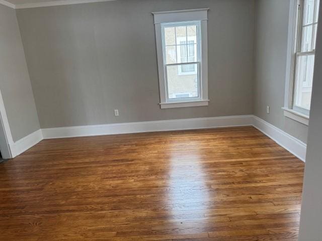 empty room featuring dark wood-type flooring, baseboards, and ornamental molding