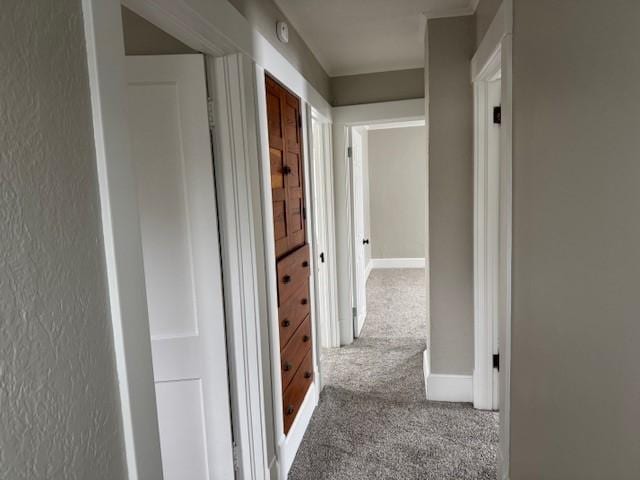 hall with carpet flooring, a textured wall, and baseboards