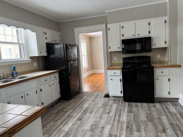 kitchen featuring black appliances, white cabinets, light wood-type flooring, and a sink