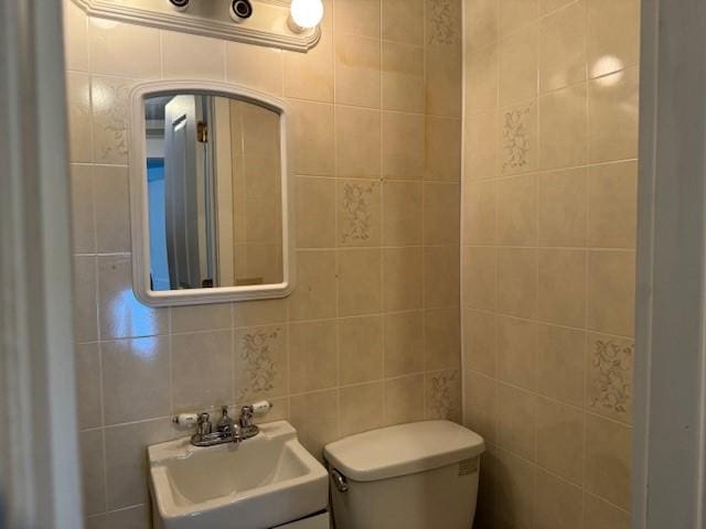 bathroom featuring toilet, tile walls, and a sink