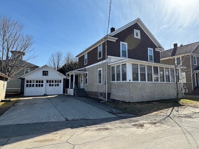 view of front of house featuring an outbuilding, a chimney, a detached garage, and a sunroom