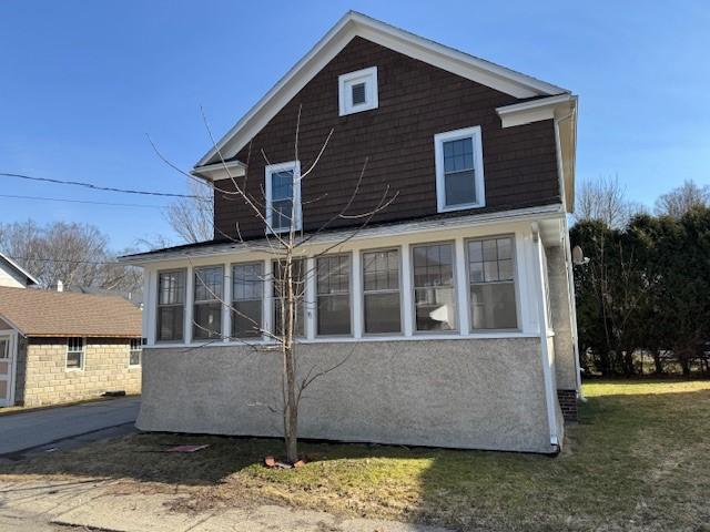 back of house with a lawn, a sunroom, and stucco siding