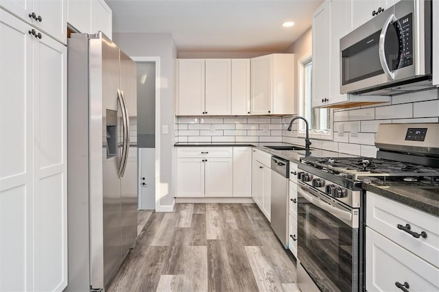 kitchen featuring sink, light wood-type flooring, dark stone countertops, stainless steel appliances, and white cabinets