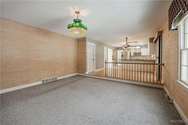 spare room featuring carpet, sink, and a chandelier