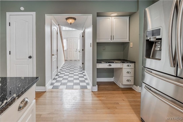 kitchen featuring built in desk, stainless steel fridge with ice dispenser, light wood-type flooring, dark stone counters, and white cabinets