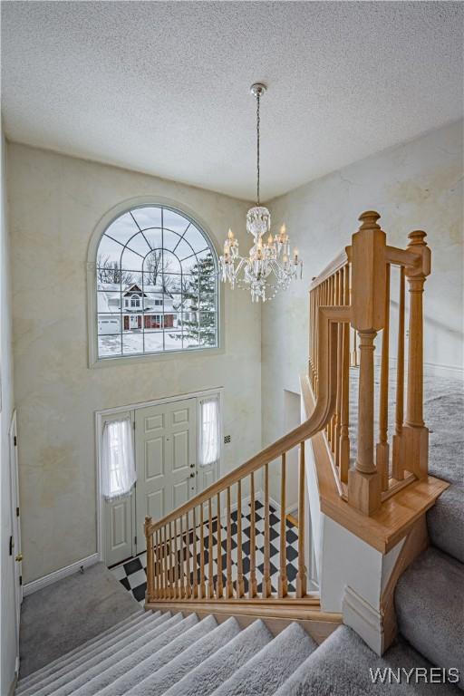 stairs featuring an inviting chandelier, carpet flooring, a wealth of natural light, and a textured ceiling