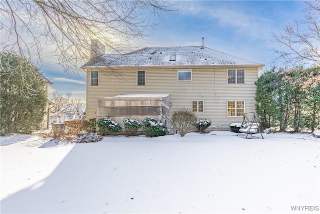 snow covered rear of property featuring a sunroom