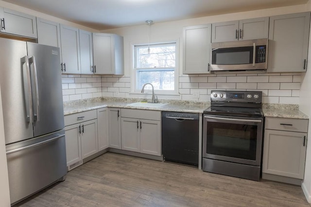 kitchen with appliances with stainless steel finishes, sink, backsplash, light stone counters, and light hardwood / wood-style flooring