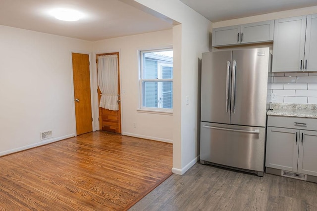 kitchen with stainless steel refrigerator, hardwood / wood-style floors, tasteful backsplash, and gray cabinetry