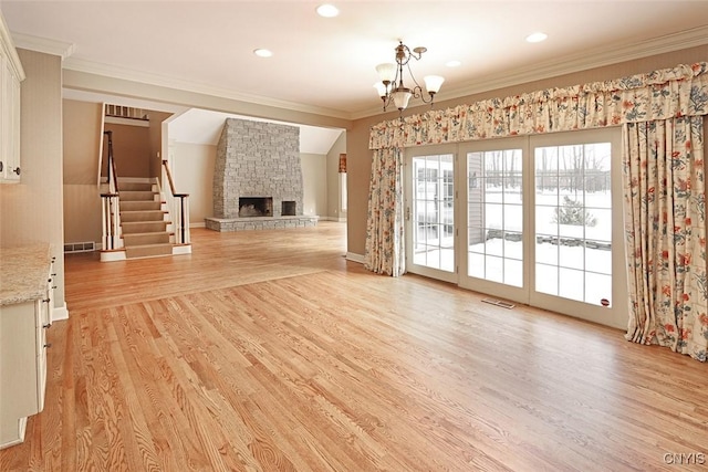 unfurnished living room featuring a notable chandelier, crown molding, a fireplace, and light wood-type flooring