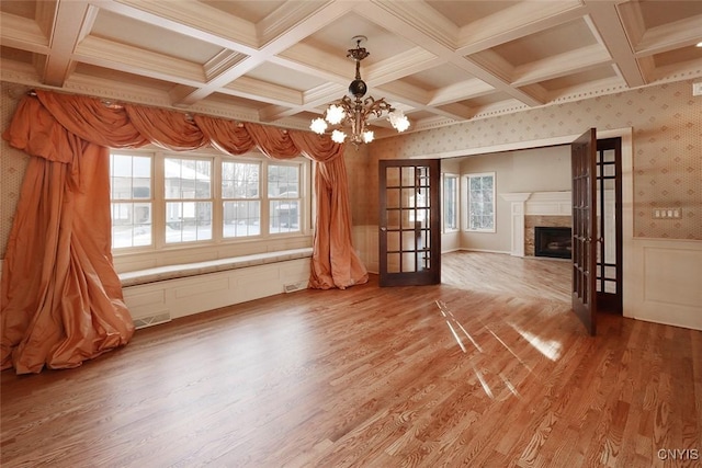 unfurnished living room with hardwood / wood-style flooring, beam ceiling, coffered ceiling, an inviting chandelier, and french doors