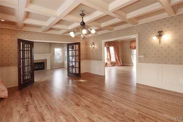 unfurnished living room featuring wood-type flooring, beam ceiling, coffered ceiling, an inviting chandelier, and french doors