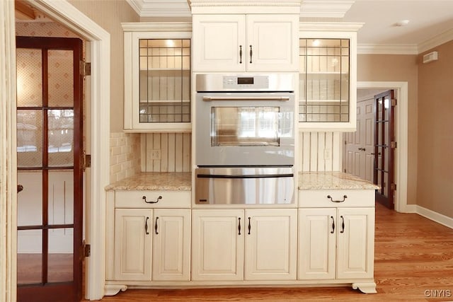 kitchen featuring white cabinetry, backsplash, light stone counters, ornamental molding, and light hardwood / wood-style floors