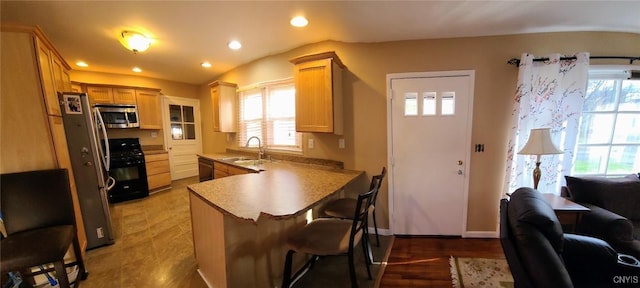 kitchen with a kitchen bar, sink, vaulted ceiling, kitchen peninsula, and black appliances