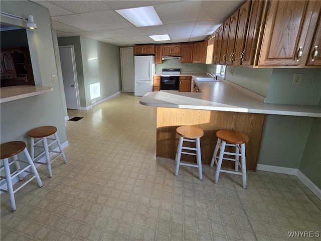 kitchen with range with electric stovetop, sink, a breakfast bar area, white refrigerator, and kitchen peninsula