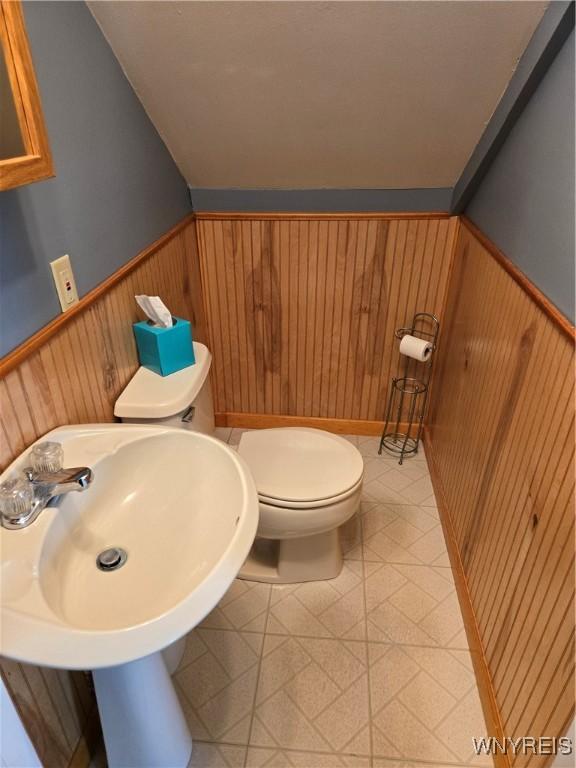 bathroom with lofted ceiling, sink, toilet, and wood walls