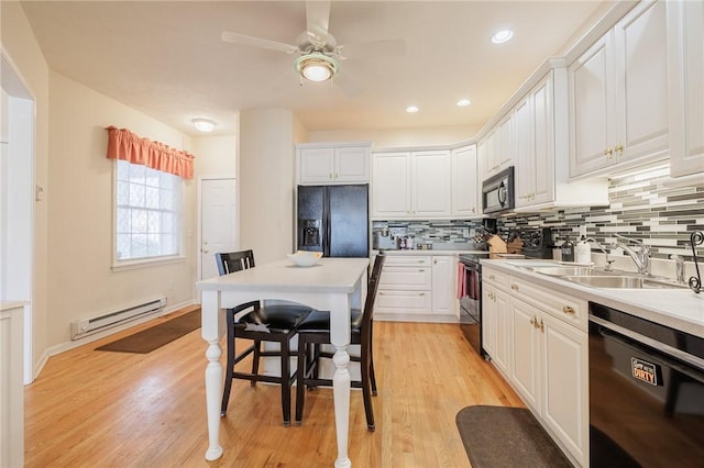 kitchen featuring sink, tasteful backsplash, black appliances, baseboard heating, and white cabinets