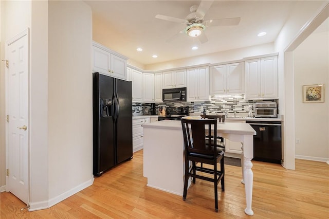 kitchen with a breakfast bar area, black appliances, a center island, decorative backsplash, and white cabinets