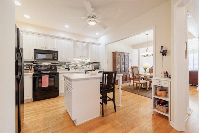 kitchen featuring a kitchen bar, black appliances, a kitchen island, pendant lighting, and white cabinets