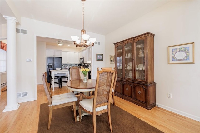 dining space with a baseboard heating unit, decorative columns, light hardwood / wood-style floors, and a chandelier