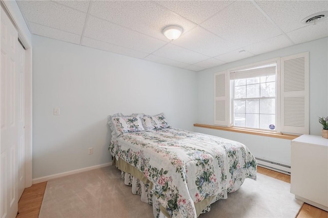 bedroom featuring a baseboard heating unit, a paneled ceiling, and light hardwood / wood-style floors